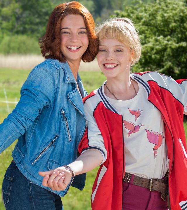 Bibi & Tina stehen auf einer Koppel und lächeln in die Kamera
