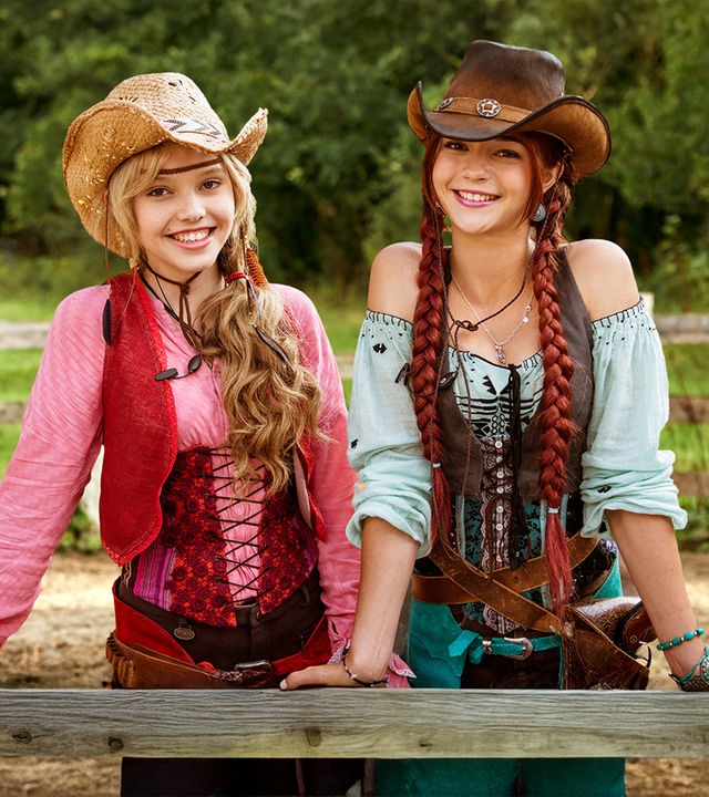 Bibi & Tina stehen auf einer Koppel, tragen Cowboy-Hüte und lächeln in die Kamera 