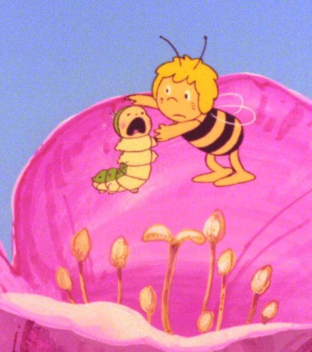 In einer großen, pinkfarbenen Blüte steht Bienenmädchen Maja und tröstet ein weinendes Raupenbaby.
