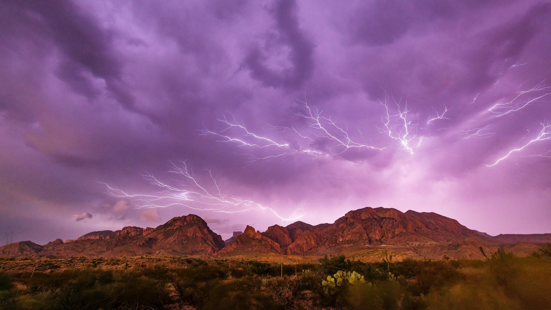 Ein lilafrabener Himmel mit weissem Blitzgewitter über einer Bergkette