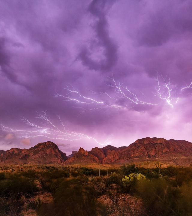 Ein lilafrabener Himmel mit weissem Blitzgewitter über einer Bergkette