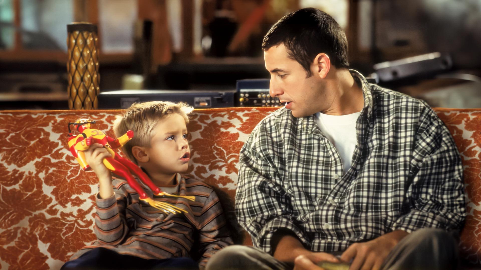 Sonny (Adam Sandler) und der kleine Julian (Cole/Dylan Sprouse) sitzen nebeneinander auf einer Couch und schauen sich an.