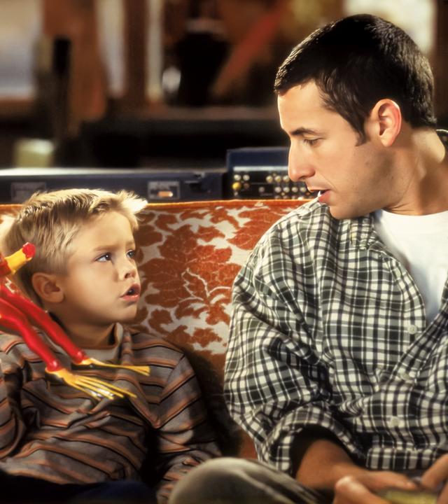 Sonny (Adam Sandler) und der kleine Julian (Cole/Dylan Sprouse) sitzen nebeneinander auf einer Couch und schauen sich an.