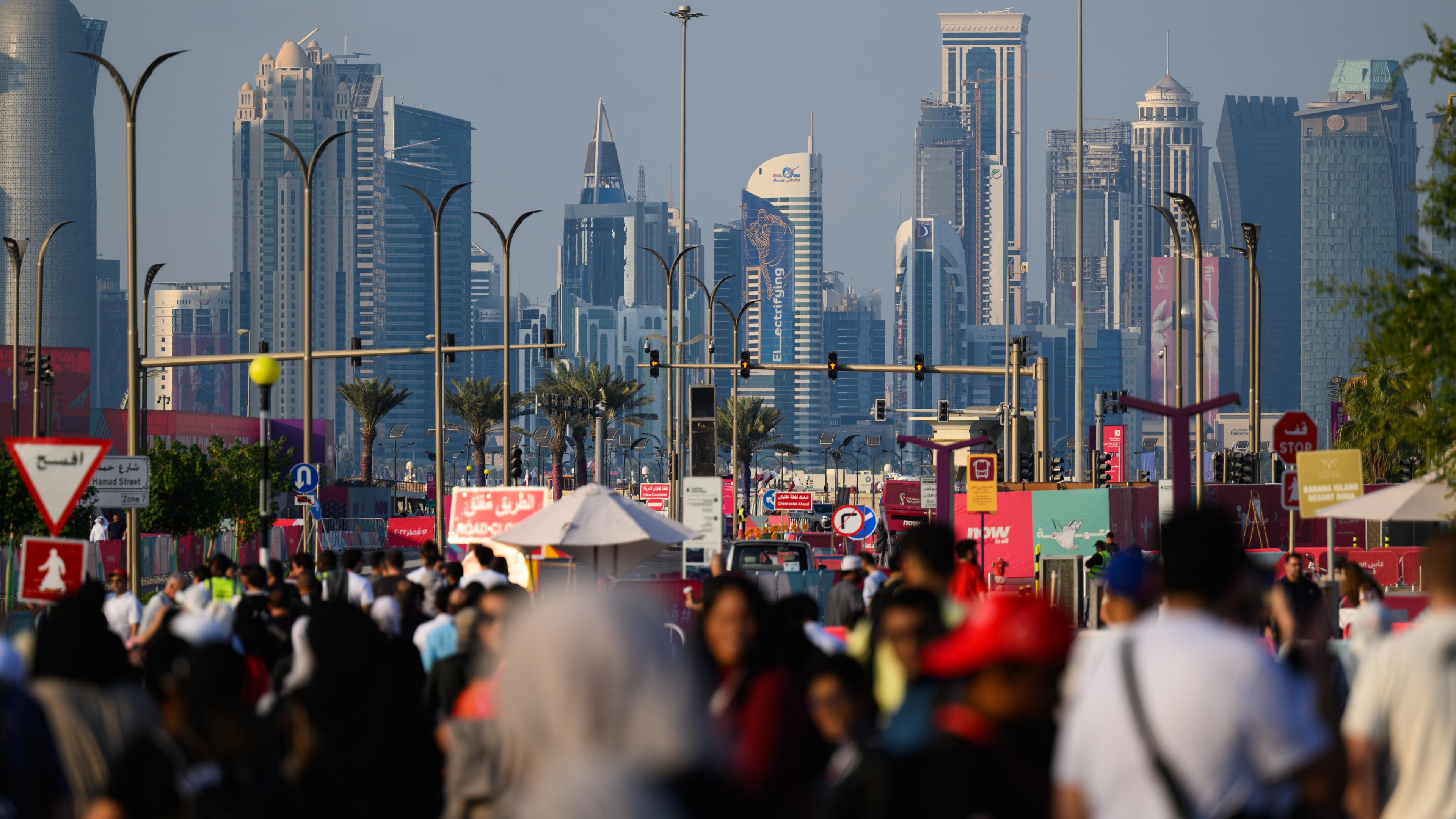 Katar, Doha: Menschen laufen am Nachmittag zum Marktplatz Souq Waqif, im Hintergrund ist die Skyline mit den modernen Hochhäusern zu sehen.