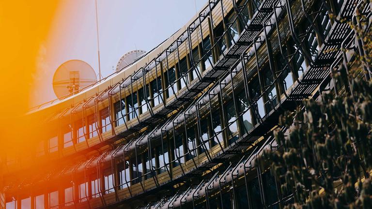 Detailaufnahme der Fensterfront des gebogenen ZDF-Sendezentrums in Mainz. Zwei Satellitenschüsseln auf dem Dach. 