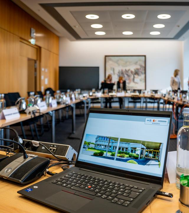 Ein Sitzungssaal mit U-förmig angeordneten Tischen, ausgestattet mit Unterlagen, Getränken und Technik, während einer Pause einer ZDF-Verwaltungsratssitzung. Einzelne Personen stehen im Hintergrund und führen Gespräche.