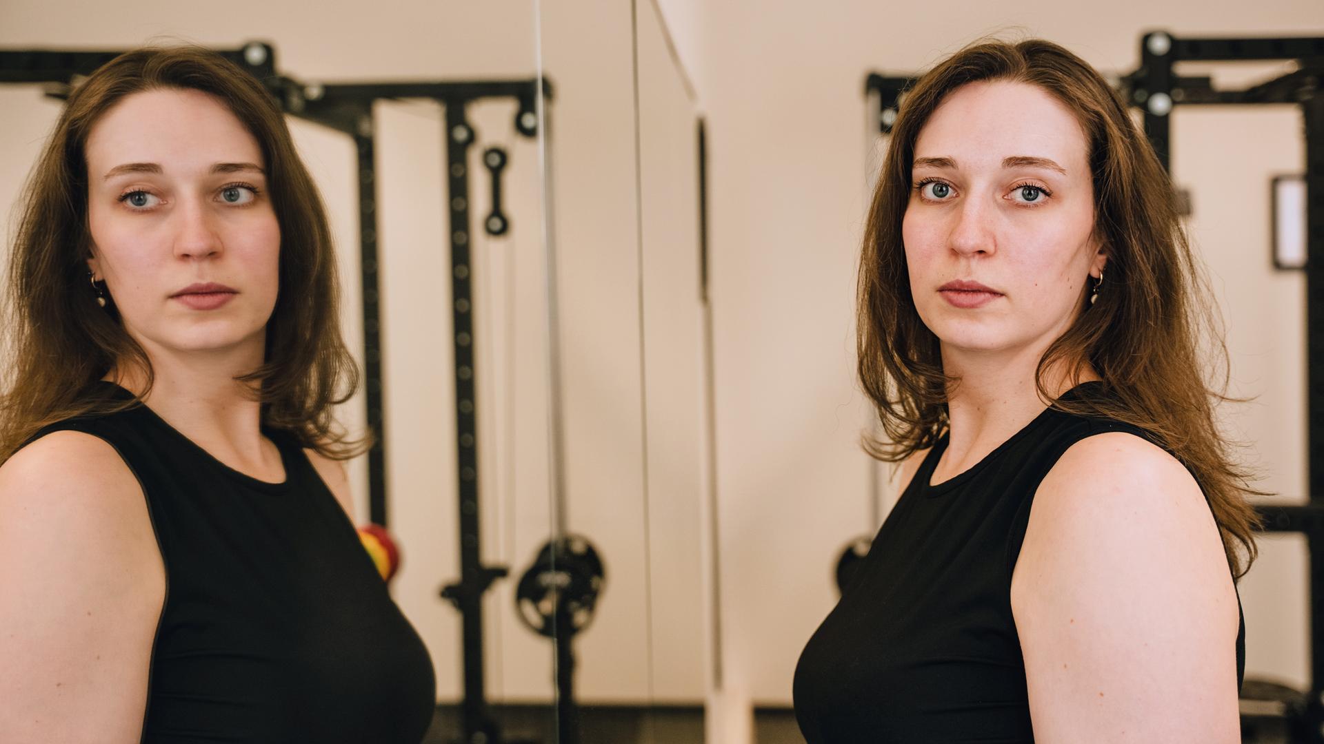 Junge Frau steht vor einem Spiegel und sieht verzweifelt aus.