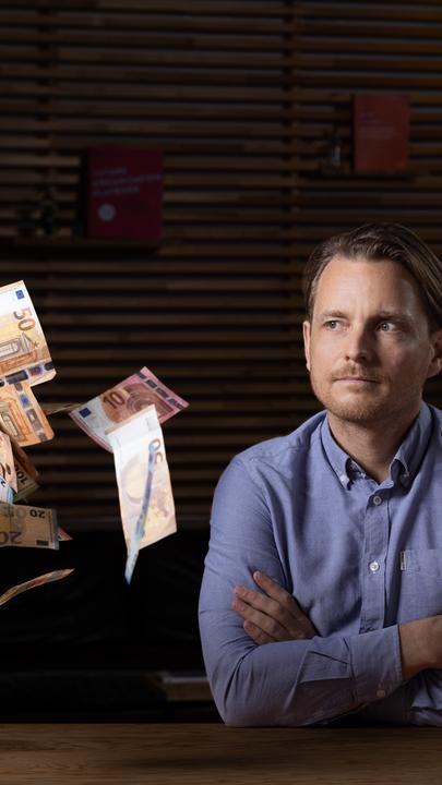 Junger Mann schaut in die Kamera, Geld fliegt umher.