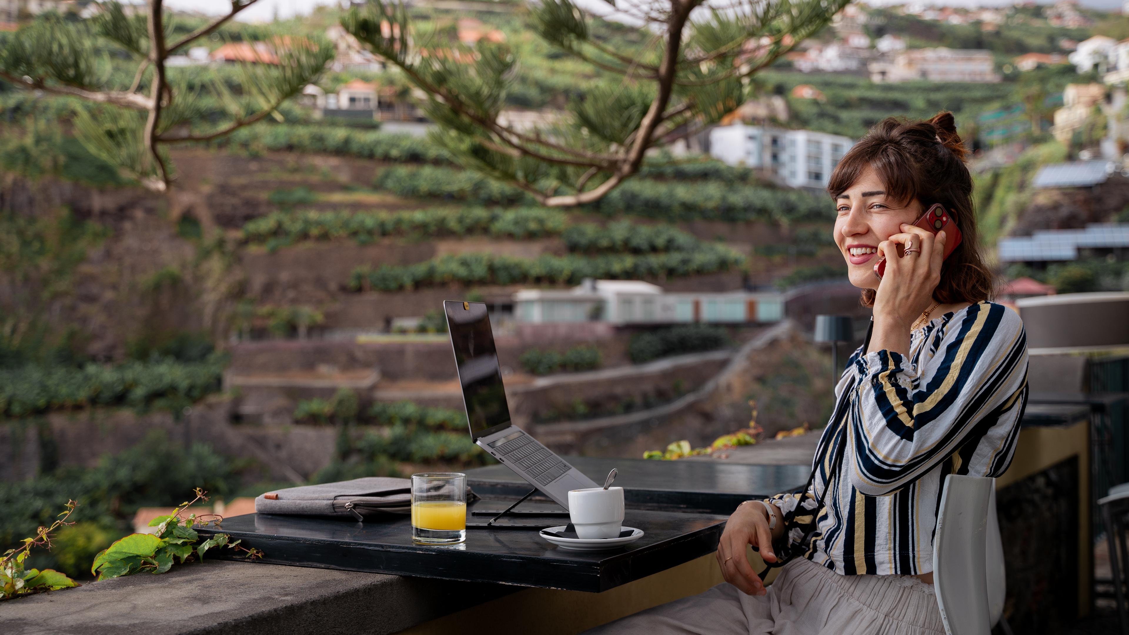 Junge Frau sitzt in der Natur an einem Tisch mit Laptop und Handy