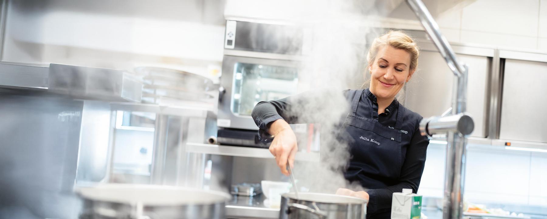 Eine junge proffessionelle Küchin hantiert am Herd