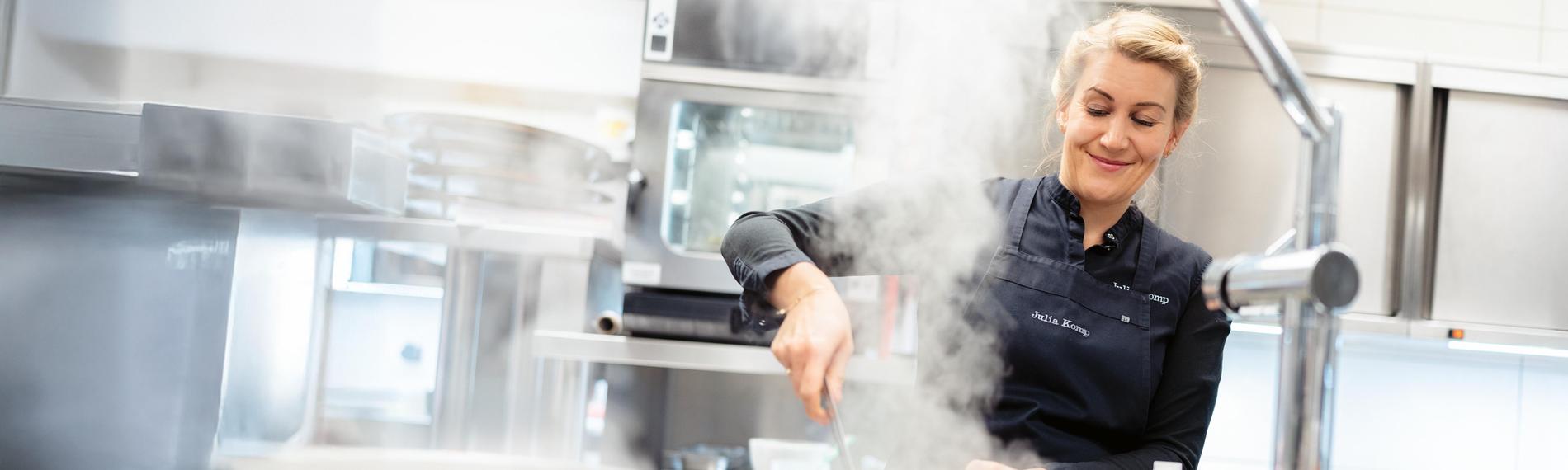 Eine junge proffessionelle Küchin hantiert am Herd