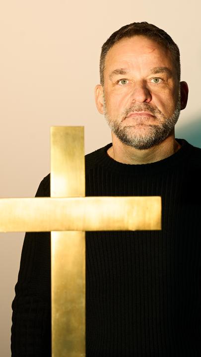 Mann steht mit ernstem Blick in einer Kirche