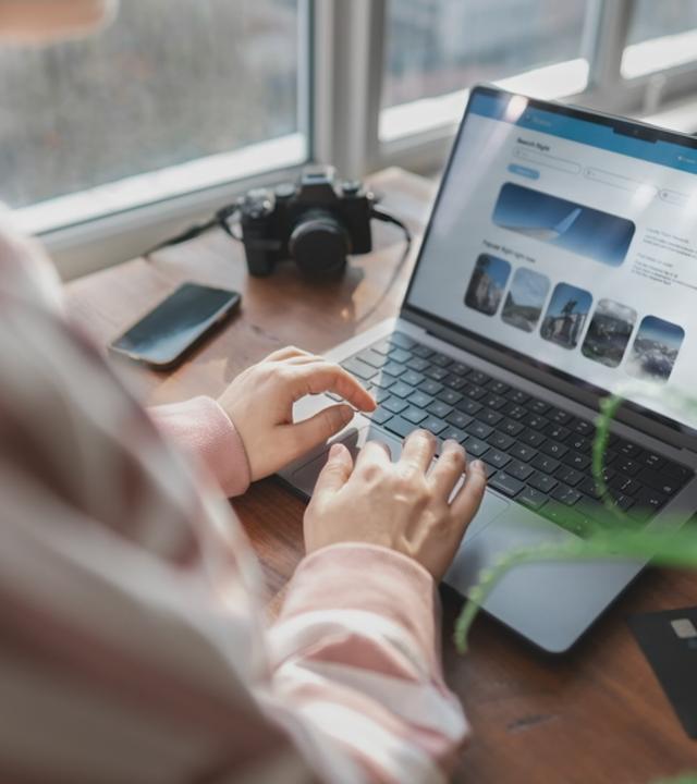 Eine Frau sitzt an ihrem Laptop. Sie ist auf einem Online-Reise-Portal unterwegs.
