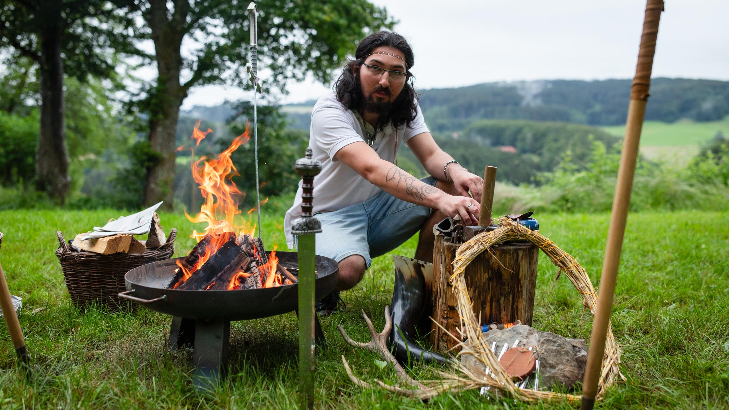 Junger Mann am Lagerfeuer mit Accecoires, die typisch für das Heidentum sind.