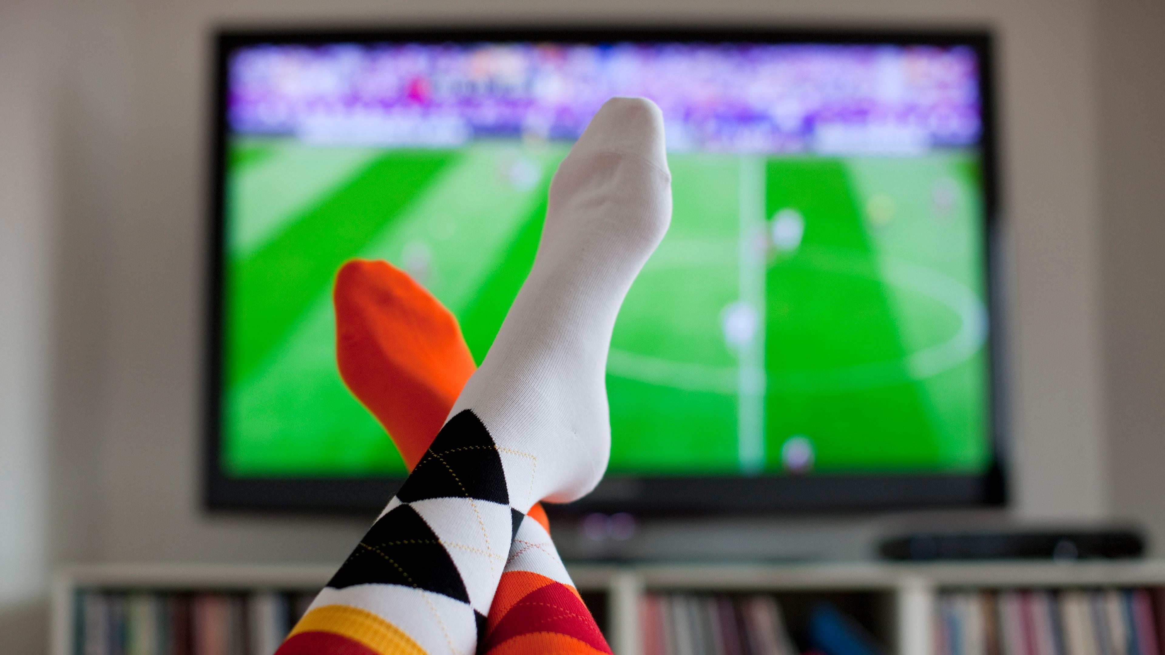 Socken von Fußballfan auf dem Tisch vor Fernseher mit Fußballspiel