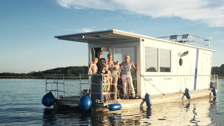 "Alles im Fluss - Leben auf dem Hausboot": ZDF-Moderatorin Barbara Hahlweg steht mit einer Familie auf einem Hausboot.