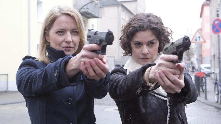 "SOKO Köln": Das Team der SOKO Köln steht nebeneinander: Die neue SOKO-Chefin Anna Maiwald (Diana Staehly, l.) mit der ebenfalls neuen Jungkommissarin Lilly Funke (Tatjana Kästel). Beide Frauen halten zielrichtend Pistolen in der Hand.