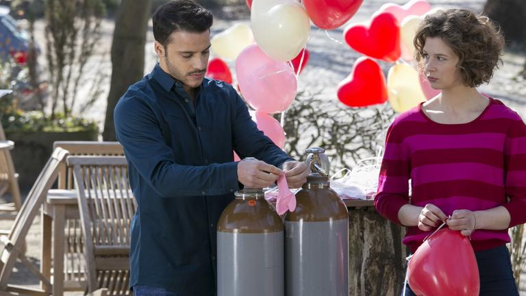 "Heiraten ist nichts für Feiglinge": Kathi (Anna Maria Sturm) und Theo (Kostja Ullmann) beim Füllen der Luftballons. Kathi schaut Theo böse an.