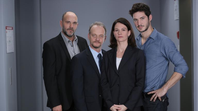 "The Killer Inside - Das Fell des Bären": Das Ermittlerteam Bob Crépault (Sylvain Marcel), Julie Beauchemin (Fanny Mallette), Maxime Moreli (Eric Bruneau) und Marcel Lévesque (Pierre Verville) stehen nebeneinander in einem Flur und blicken in die Kamera.