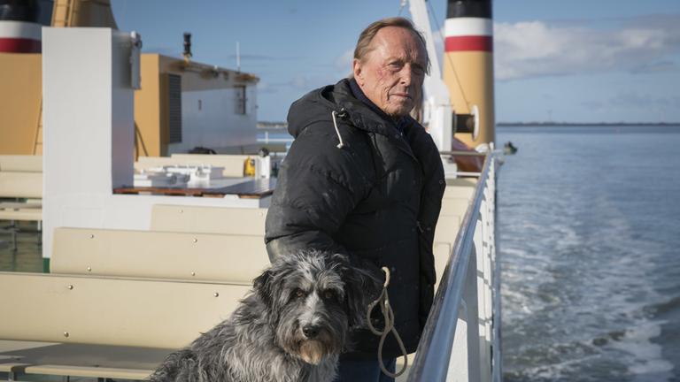 "Matula": Privatdetektiv Matula (Claus Theo Gärtner) steht auf dem Deck einer Fähre mit Hund Dr. Renz an der Leine.