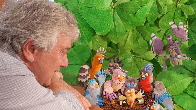 "Rolfs neue Vogelhochzeit": Rolf Zuckowski blickt in ein Neast mit Vogelfiguren