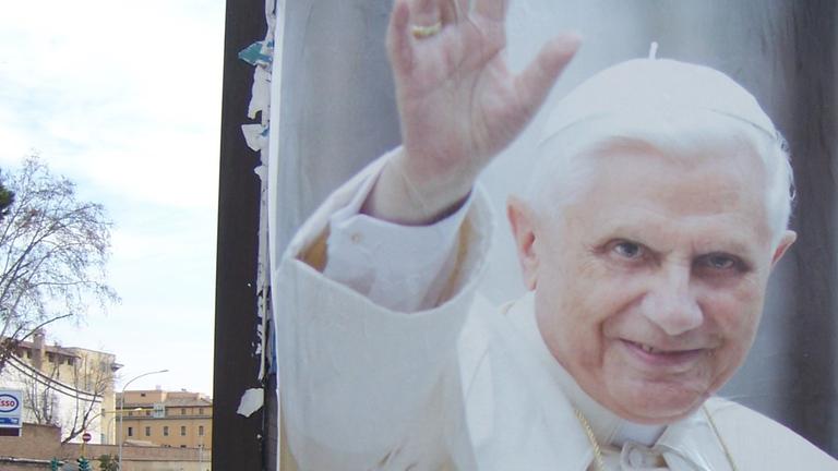 "Mitarbeiter der Wahrheit - Benedikt XVI. wird 90": Aufnahme eines Plakats auf einer römischen Straße, das Papst Benedikt XVI. zeigt. Darauf steht mit italienischem Text "Du wirst immer bei uns bleiben, Danke!".