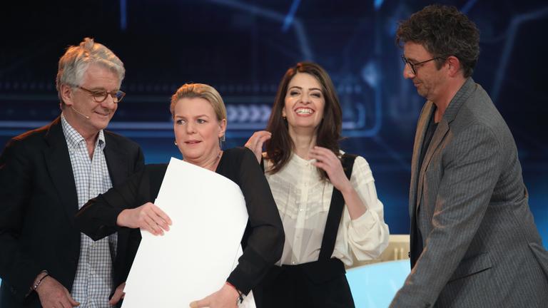 "Mich täuscht keiner!": Mirja Boes, Marcel Reif, Linda Zervakis und Hans Sigl (von links). Alle vier lachen. Mirja Boes hat mehrere große Papierbögen im Arm, die sie mit beiden Händen an ihren Körper presst.