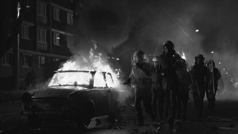 "Wir sind jung. Wir sind stark": Die Polizei läuft an einem brennenden Auto vorbei.