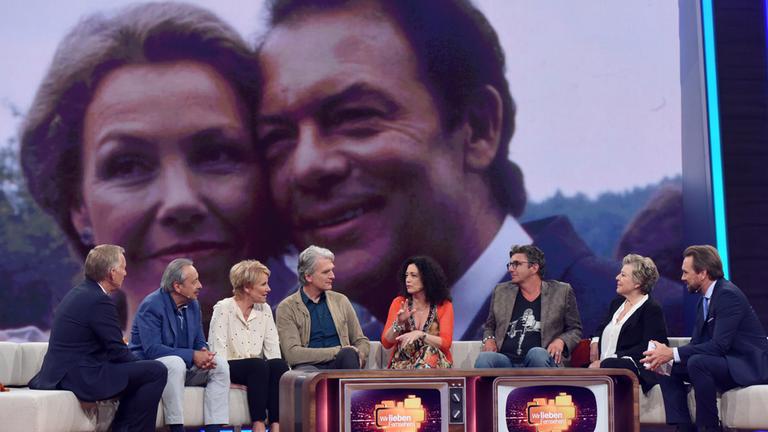 "Wir lieben Fernsehen! - Unsere größten Film- und Serienstars": Johannes B. Kerner, Wolfgang Stumph, Mariele Millowitsch, Walter Sittler, Barbara Wussow, Hans Sigl, Marie-Luise Marjan und Steven Gätjen sitzen nebeneinander auf dem Showsofa. Im Hintergrund ist auf der Videoleinwand ein Bild von Gaby Dohm und Klausjürgen Wussow zu sehen.