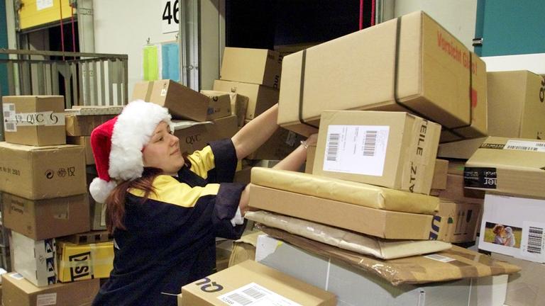 "ZDFzeit - DHL, Hermes & Co.": Eine Frau mit Weihnachtsmütze stapelt Pakete.