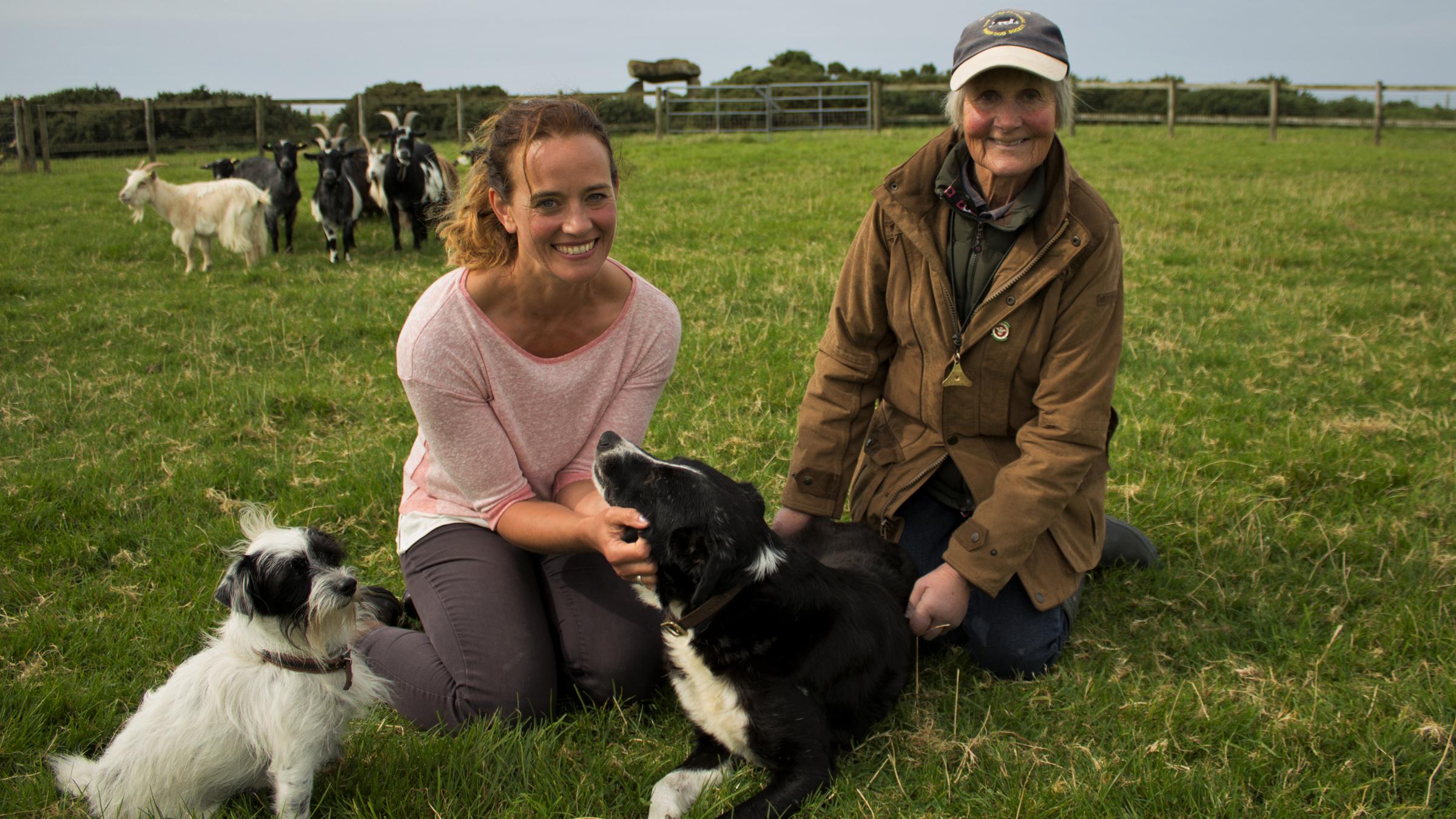"Tierisch britisch! Unterwegs mit Kate Kitchenham": Kate Kitchenham und Anna Lou Daybell knien lächelnd mit ihren zwei Hunden auf einer Wiese.
