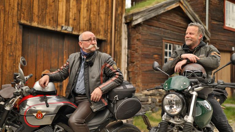 "Horst Lichter sucht das Glück": Horst Lichter und Jenke von Wilmsdorff sitzen in Motorradkleidung auf zwei abgestellten Motorrädern. Im Hintergrund sind Holzhäuser zu sehen.