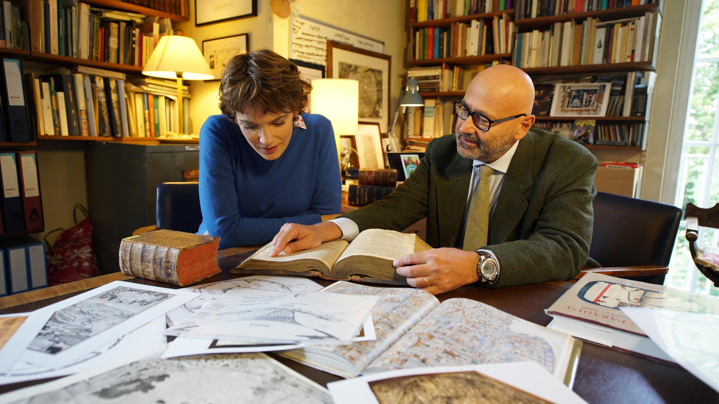 "Die Suche nach dem Paradies": Lena Ganschow und Alessandro Scafi sitzen gemeinsam an einem Schreibtisch und schauen sich antike Bücher und Karten an.