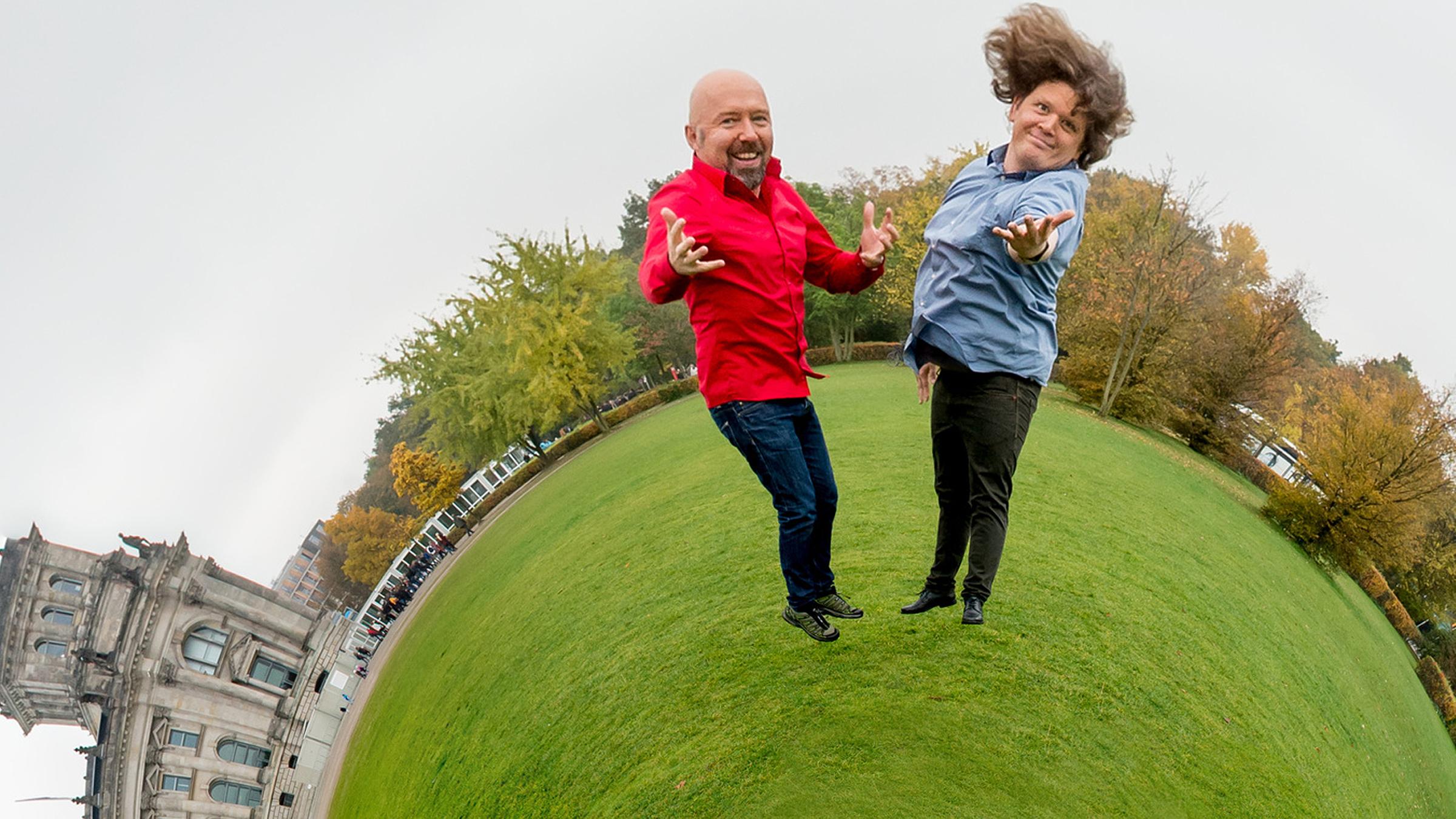 "Der satirische Jahresrückblick 2017": Die Satire-Autoren Andreas Wiemers und Werner Doyé stehen mit einladender Geste vor dem Reichstagsgebäude. Die Erde unter ihren Füßen ist zu einer kleinen Kugel geschrumpft.