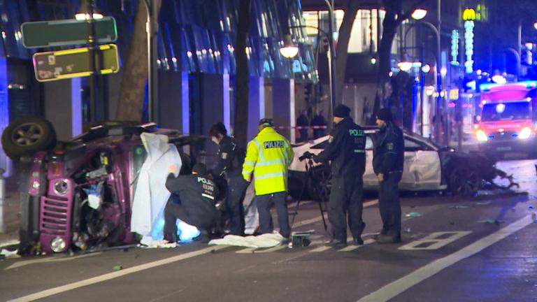 "ZDF.reportage: Illegale Autorennen - Mit Tempo 100 durch die Stadt": Polizeibeamte sichern ein auf der Seite liegendes, demoliertes Auto. Im Hintergrund steht ein weiteres eingedelltes Auto sowie ein Krankenwagen.