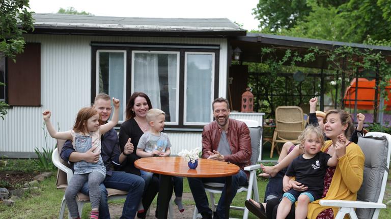 "WISO-Dokumentation: Mein Traumurlaub - Wie die Deutschen verreisen": Zwei Familien sitzen an einem Tisch vor einem Campinghäuschen. Zwischen ihnen Moderator Marcus Niehaves.