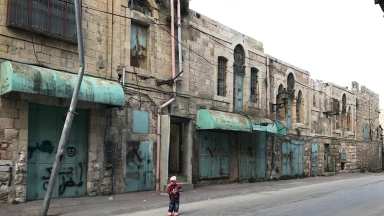  "auslandsjournal - die doku: Hebron - Die zerrissene Stadt - 50 Jahre nach dem Sechstagekrieg": kleines Kind steht in einer Straße vor geschlossenen Geschäften.