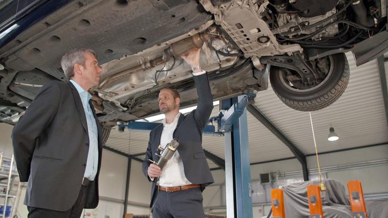 "ZDFzoom: Geheimakte VW": Marcus Hauser von der Baumot AG schaut sich mit dem Autor die Unterseite eines Autos an.