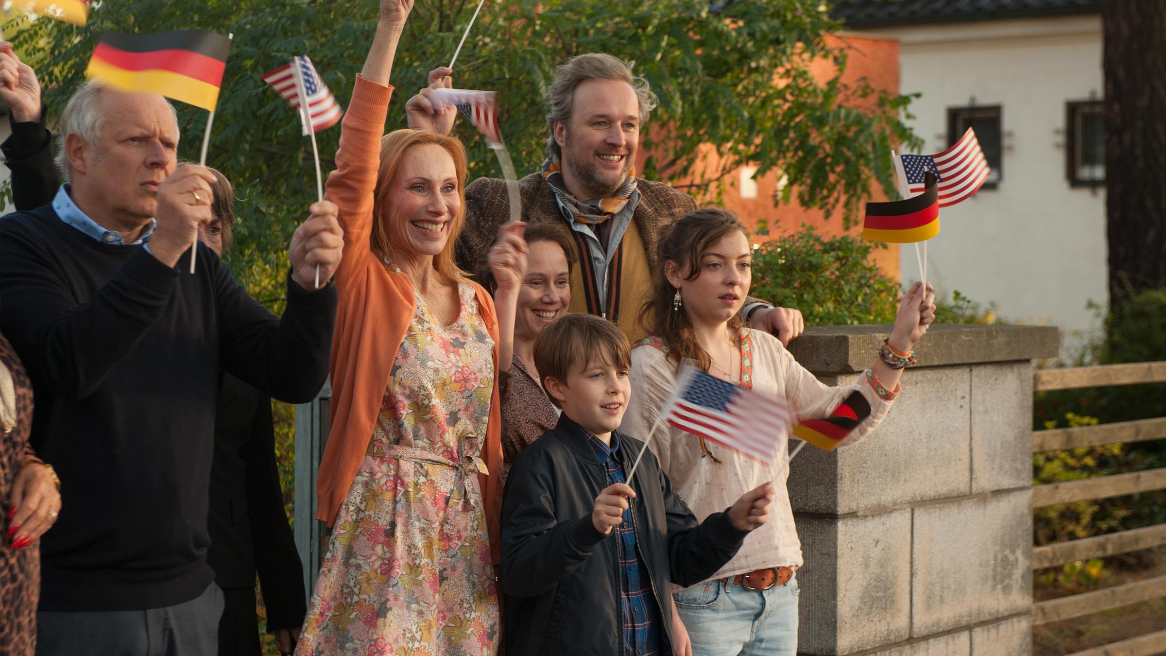 "Ihr seid natürlich eingeladen": Gerald (Axel Milberg), Ilse (Thekla Carola Wied), Gundula (Andrea Sawatzki), Matz (Mathis Wernecke), Rose (Eva Löbau), Ricarda (Amber M. Bongard) und Hadi (Stephan Grossmann) stehen am Gartentürchen und wedeln mit bunten Papierfähnchen.