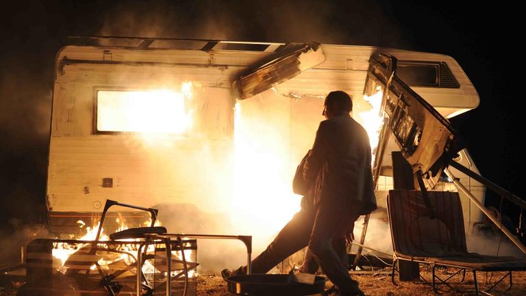 "Spreewaldkrimi - Zwischen Tod und Leben": Das brennende Wohnmobil von Kommissar Krüger (Christian Redl). Im Vordergrund wird er von er von einem Mann von den Flammen weggezogen.