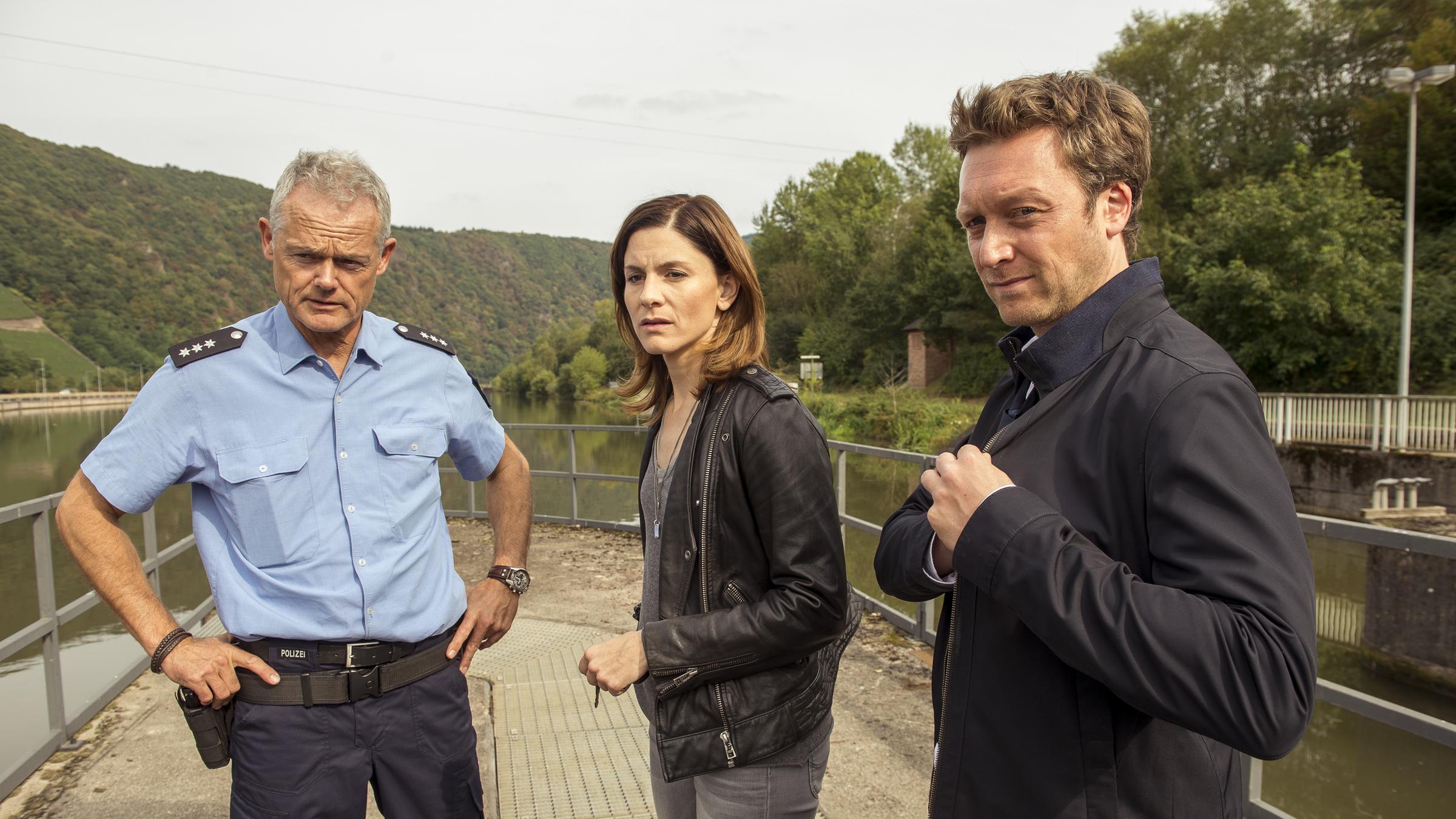 "In Wahrheit – Mord am Engelsgraben": Ein Polizist (Komparse), Judith Mohn (Christina Hecke) und Freddy Breyer (Robin Sondermann) stehen nebeneinander und schauen in die gleiche Richtung.