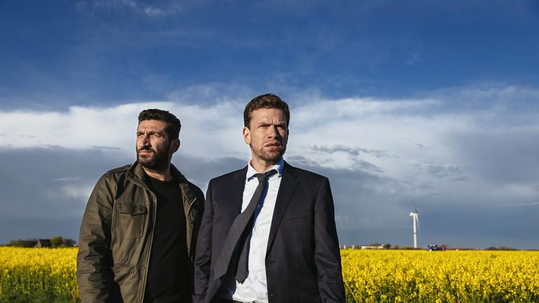 "Jussi Adler-Olsen: Erlösung": Assad (Fares Fares) und sein Kollege Carl (Nikolaj Lie Kaas) stehen vor einem blühenden Rapsfeld.