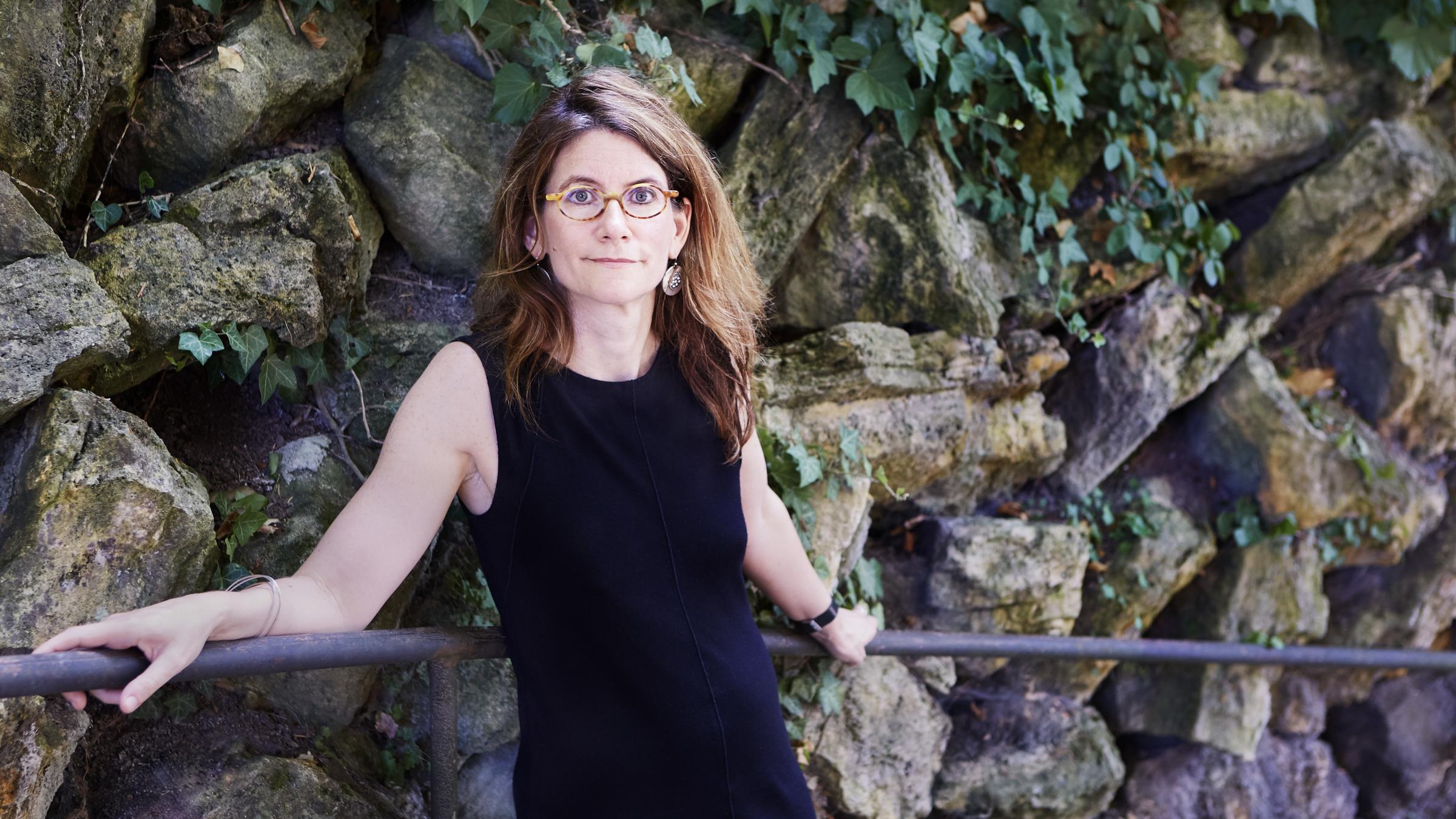 Anna Katharina Hahn ist an ein Geländer gelähnt, sie trägt ein schwarzes, ärmelloses Kleid. Im Hintergrund eine Felswand.