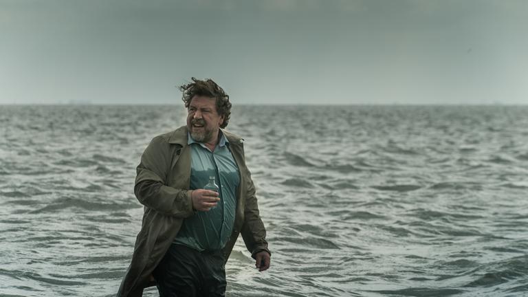 "Der gute Bulle": Fredo Schulz (Armin Rohde) steht mit einer Flasche Alkohol und komplett angezogen bis zu den Knien im Meer.