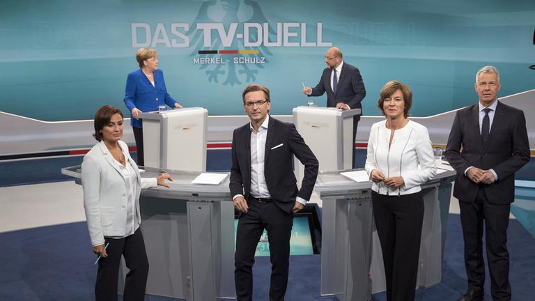 "Das TV-Duell Merkel-Schulz" (3.9.2017): hinten Bundeskanzlerin Angela Merkel und ihr Herausforderer Martin Schulz vorne das Moderatorenteam Sandra Maischberger (ARD), Claus Strunz (ProSieben/SAT.1)Maybrit Illner (ZDF) und Peter Kloeppel (RTL)