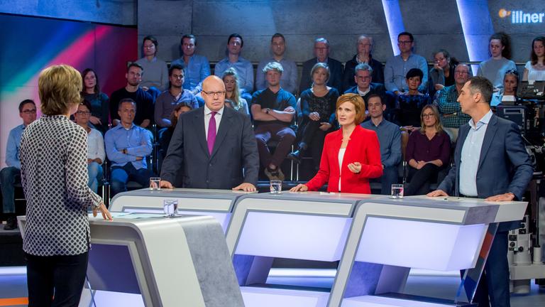 "Illner intensiv": Peter Altmaier(CDU),  Katja Kipping (Die Linke) und Cem Özdemir (Die Grünen) stehen nebeneinander am Pult im Studio; Im Hindergrund Zuschauer; gegenüber steht Maybrit Illneer am Pult.