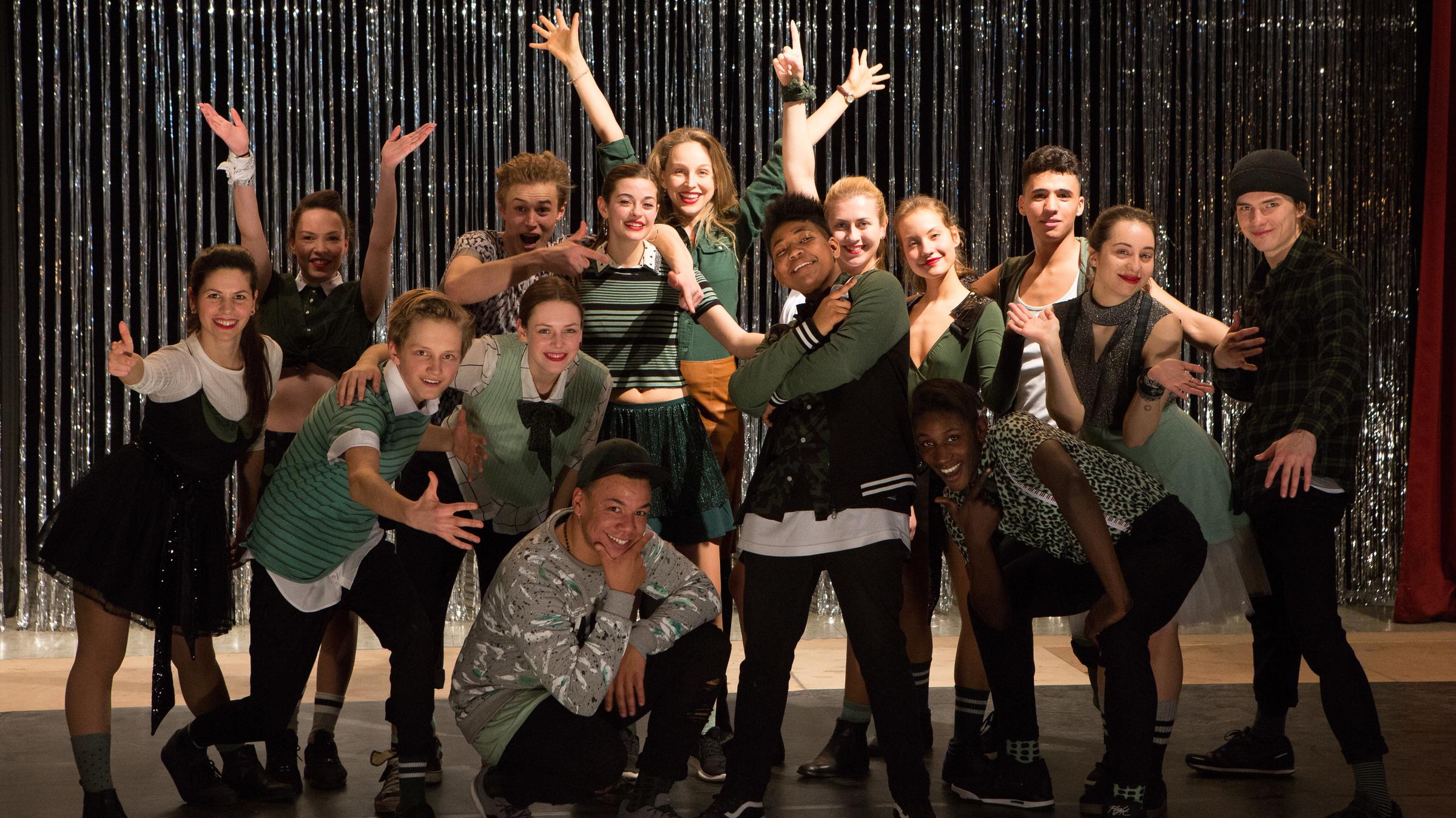 "Wir lieben das Leben": die Lehrerin Maria Kowalke (Petra Schmidt-Schaller) steht inmitten ihrer Schulklasse nach der Abschlussaufführung auf der Bühne der Aula.