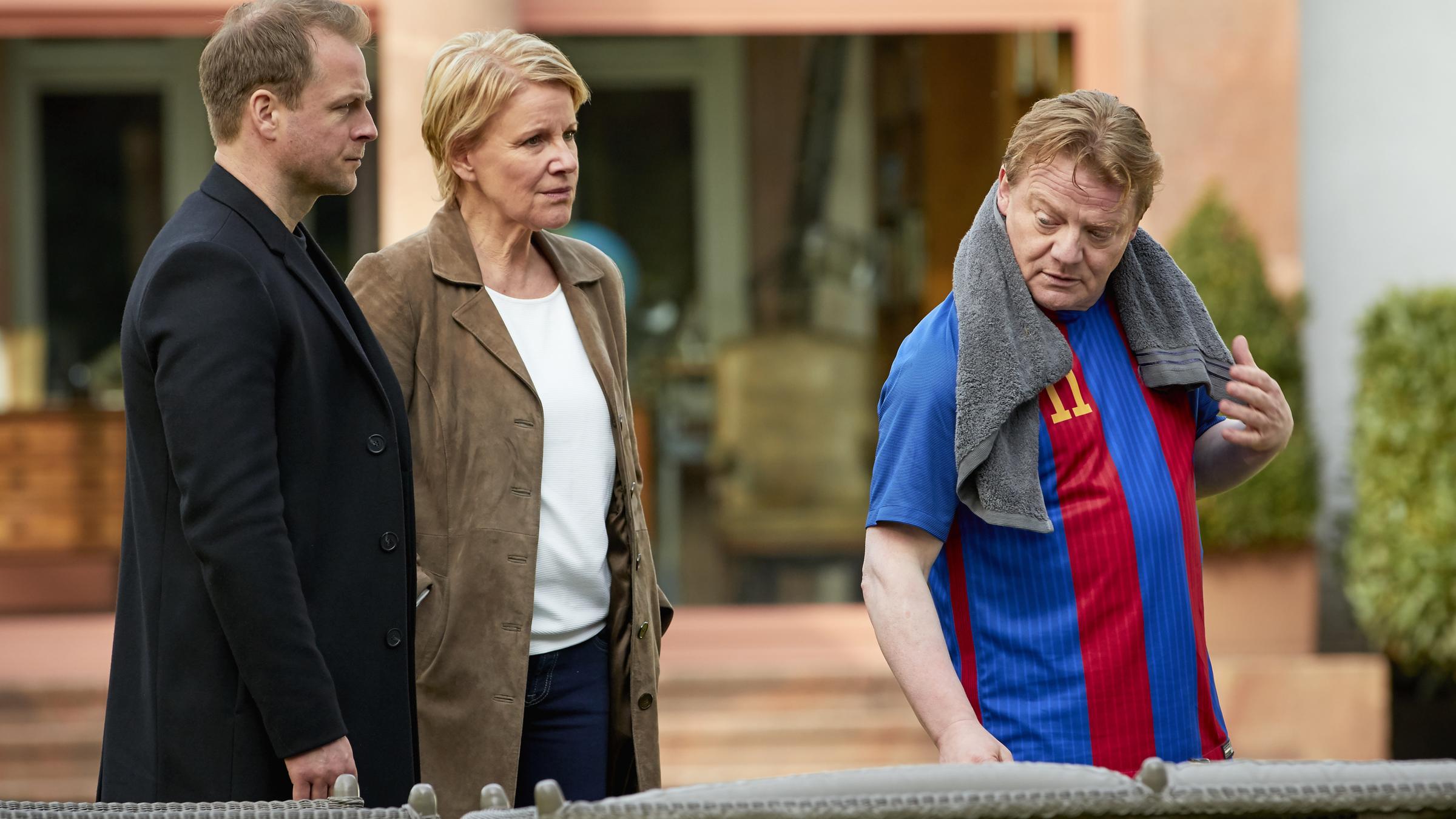 "Marie Brand und der schwarze Tag": Marie Brand (Mariele Millowitsch) und Simmel (Hinnerk Schönemann) befragen Christian Grave (Werner Wölbern) in dessen Garten. Grave hat ein Fußball-Trikot an und ein Handtuch liegt um seinen Hals.