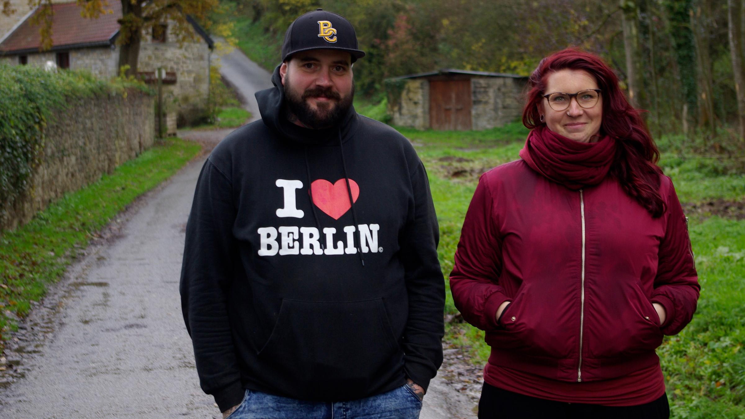 "37°: Nach dem Anschlag - Terroropfer auf ihrem Weg zurück ins Leben": Julia und Thomas Schmitz gehen nebeneinander einen Waldweg entlang. Im Hintergrund sind kleine Steinhäuser zu erkennen.