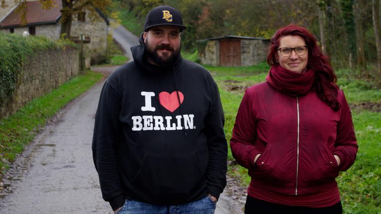 "37°: Nach dem Anschlag - Terroropfer auf ihrem Weg zurück ins Leben": Julia und Thomas Schmitz gehen nebeneinander einen Waldweg entlang. Im Hintergrund sind kleine Steinhäuser zu erkennen.